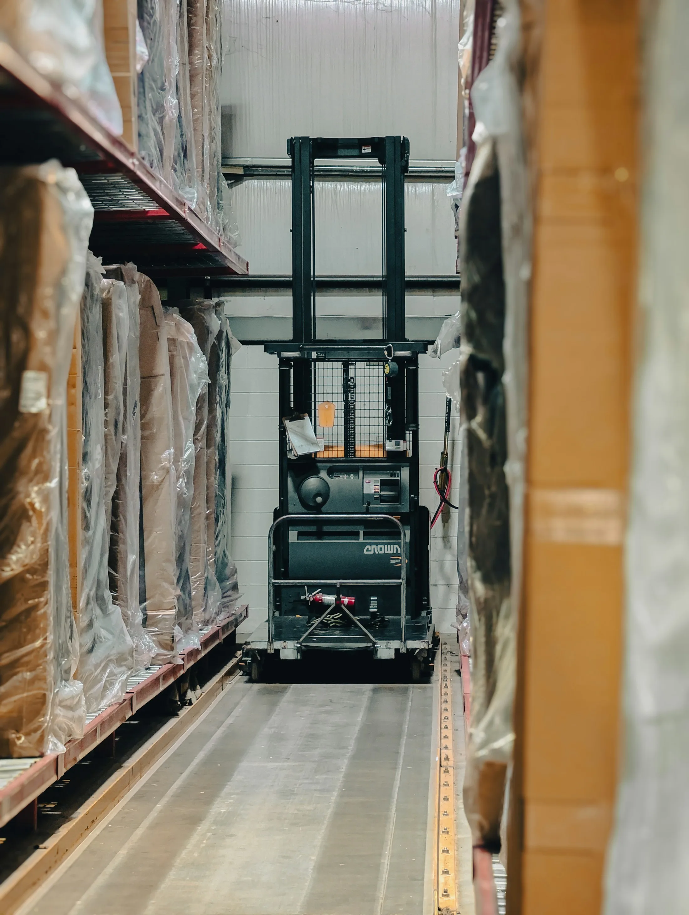 Forklift positioned between warehouse racks of wrapped pallet loads